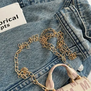 Close-up detail of a stylish mini luxury crossbody bag with gold chain on denim fabric.