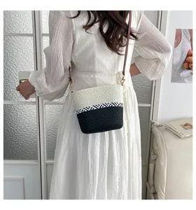 Primer plano de un bolso de paja trenzado en bloques de color usado cruzado con un vestido blanco