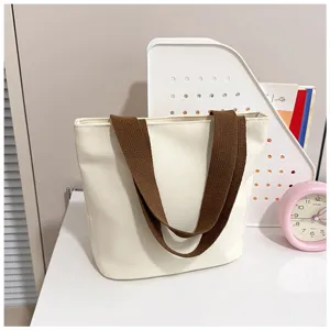 Bolso tote minimalista de lona crema con correas marrones sobre un escritorio organizado