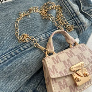 Detail view of a luxury mini crossbody handbag with gold chain strap and M-pattern design