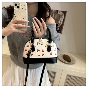Nahaufnahme einer weißen Muschelhandtasche mit rotem Kirschmuster und schwarzen Tragegriffen