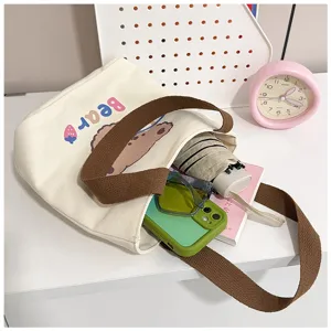 Vista detallada de un bolso tote de lona blanco con estampado de oso y gran capacidad