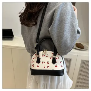 Detailansicht einer weißen Handtasche mit Kirschdruck, schwarzen Akzenten und Gurt