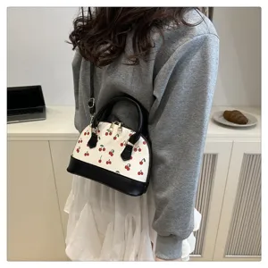 Detailansicht einer stylischen weißen Kirschprint-Muscheltasche, getragen zum grauen Sweatshirt