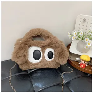 Detalle de bolso de peluche marrón con ojos grandes y correa de cadena metálica dorada.