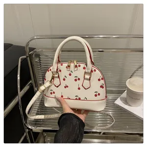 Detailaufnahme der weißen Muscheltasche mit rotem Kirschmuster und rotem Besatz.