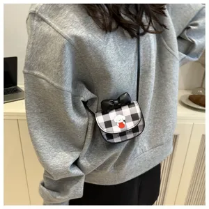 Detalle de un mini bolso bandolera de cuadros con estampado de dibujos y un lazo negro