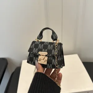 Macro detail of a mini black crossbody bag featuring silver monogram and gold chain strap