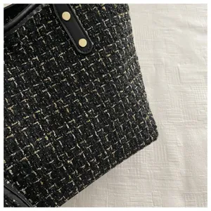 Detailopname van zwart-gouden wollen tweed textuur en lederen rand aan een handtasje
