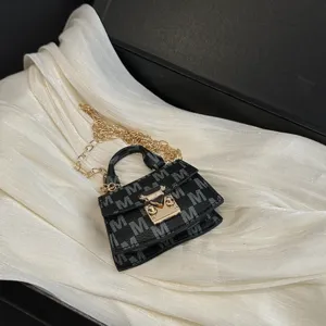 Close-up detail of luxury mini crossbody accessory bag with M-pattern and gold chain strap