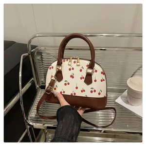 Detail einer Shell-Handtasche mit Kirschprint, braunem Besatz und Griffen
