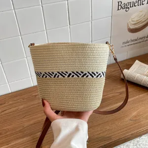 Bolso cubo de paja tejida con diseño geométrico blanco y negro y correa marrón.