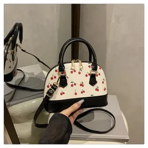 Detailansicht einer weißen Handtasche mit rotem Kirschmuster und schwarzem Trageriemen