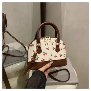Detailansicht einer muschelförmigen Handtasche mit Kirschmuster und braunem Besatz