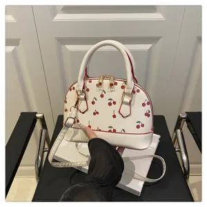 Nahaufnahme einer weißen Muschel-Handtasche mit süßem Kirschprint und Golddetails