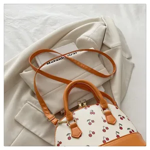 Detailansicht der stylischen cremefarbenen Tasche mit Kirschmuster und orangen Griffen