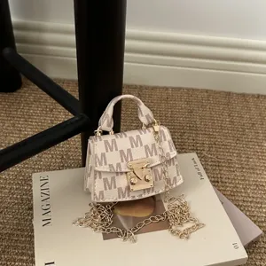 Detail of luxury miniature crossbody bag with M pattern and golden metal chain strap