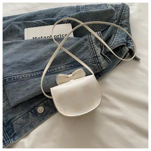 Elegante mini bolso bandolera blanco con patrón de cuadros y lazo sobre chaqueta vaquera