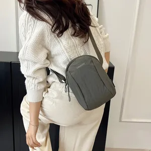 Bolso bandolera informal de nailon verde oscuro impermeable sobre un jersey blanco.