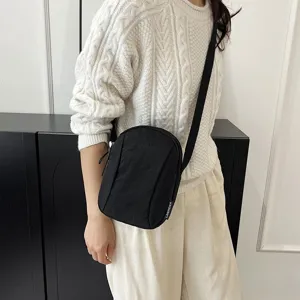Detalle de un bolso bandolera negro de nailon minimalista sobre un jersey blanco