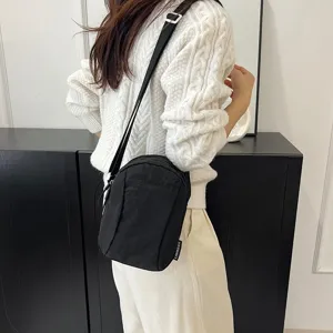 Bolso bandolera de nailon negro llevado sobre un suéter de punto blanco