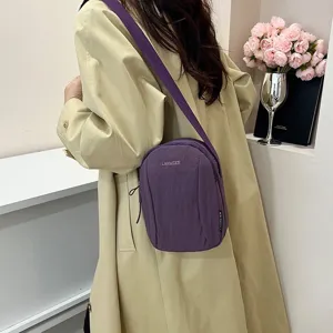 Detalle de un bolso bandolera de nailon morado con una gabardina beige