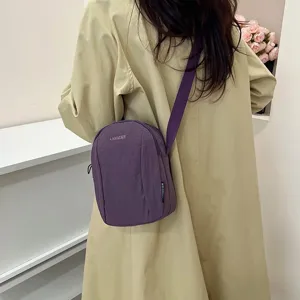 Detalle de bolso bandolera de nailon violeta impermeable con gabardina casual