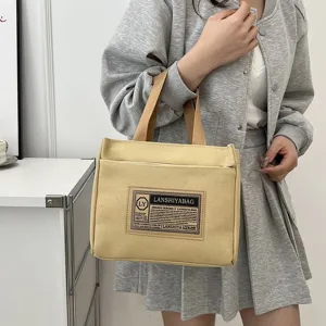 Detailed view of beige canvas tote bag showing the front pocket and design label