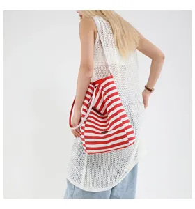 Vista detallada de un gran bolso de lona con rayas rojas y blancas llevado por modelo.