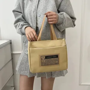 Close-up of yellow canvas commuter tote bag held by person in casual outfit