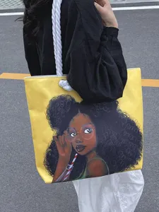 Detalle de un bolso tote amarillo con estampado de chica negra y asas de cuerda.