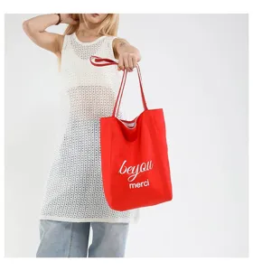 Primer plano de un bolso tote de lona rojo vibrante sostenido por una modelo