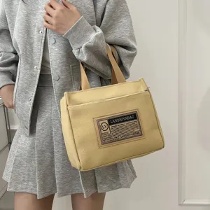 Detail of a mustard yellow canvas handbag held by a model in a grey outfit.