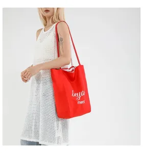 Modelo llevando un gran bolso tote de lona roja con detalle de letras merci blancas