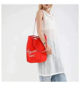 Modelo con un gran bolso de compras de lona roja con estampado del eslogan 'merci'
