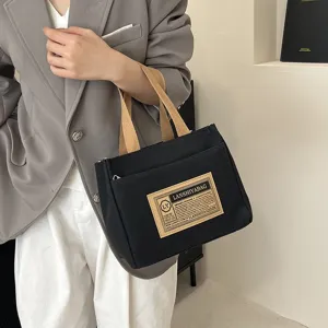 Close-up of the black canvas commuter tote bag featuring a stylish logo patch detail