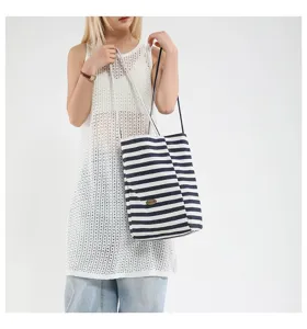 Modelo asiática luciendo un bolso tote de lona a rayas azul marino en un estilo casual