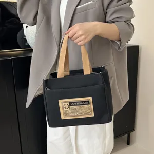 Detailed close-up of a black canvas handbag with brown woven handles and a vintage label
