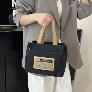 Close-up detail of the black canvas handbag with a vintage logo label and khaki handles