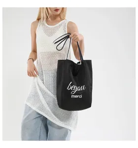 Bolso tote de lona negra con estampado 'beyou merci' mostrado por una modelo.