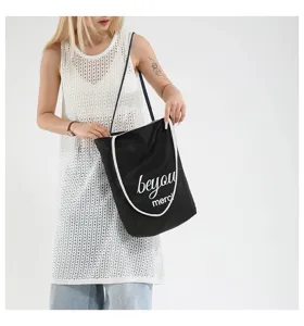 Detalle de un bolso tote de lona negra con estampado 'beyou merci' llevado por una modelo.