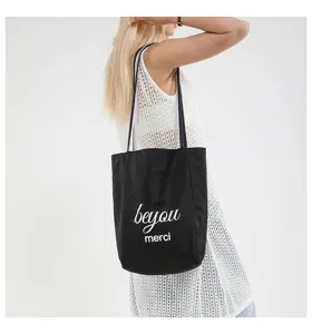 Bolso tote de lona negra de moda con letras blancas llevado por una modelo