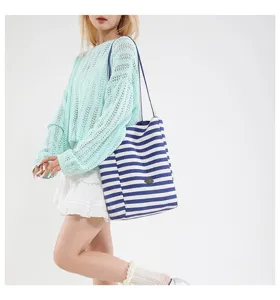 Bolso tote de lona a rayas azules y blancas de gran capacidad llevado al hombro por una modelo
