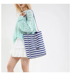 Detalle de un bolso tote grande de lona a rayas azules y blancas en una modelo.