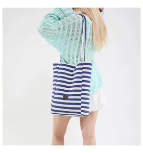 Detalle de un bolso tote de lona con rayas azules y blancas llevado al hombro.