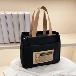 Detail view of a black canvas lunch tote bag with beige handles and label