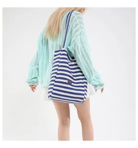 Bolso tote de lona a rayas azules y blancas, detalle mostrado en la espalda del modelo.