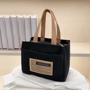 Close-up detail of a minimalist black canvas lunch bag with a decorative stitched label