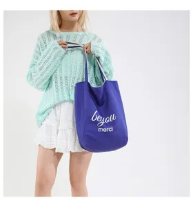 Bolso de lona azul grande con estampado merci blanco llevado por una modelo femenina