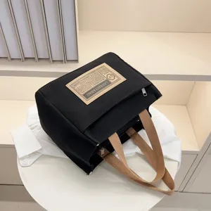 Stylish black canvas lunch bag with brown handles displayed on a white display table
